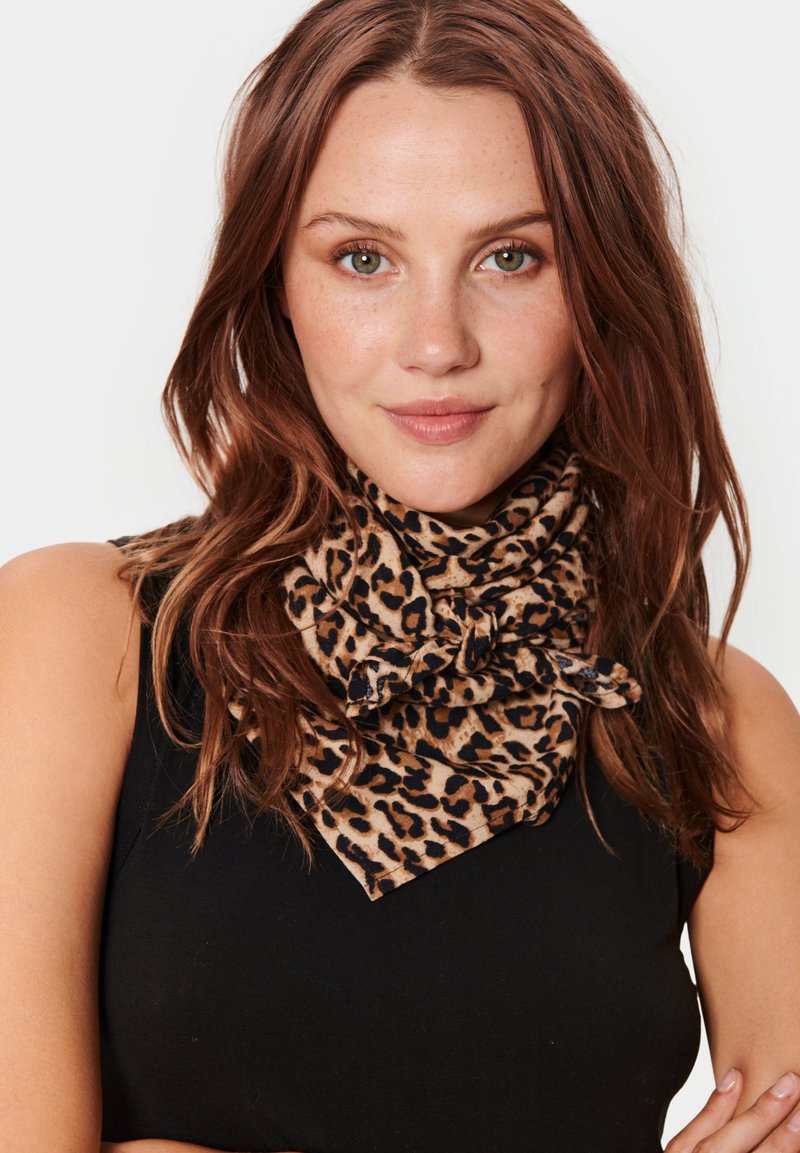 Barna és fekete állatmintás sál, nyakban megkötve. Puha tapintású, háromszögletű forma, fekete ujjatlan felsőhöz viselve.