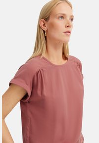 Rosenfarbenes Blusenshirt mit kurzen, aufgerollten Ärmeln, rundem Ausschnitt und dezenten Falten an den Schultern. Glatter, leichter Stoff.