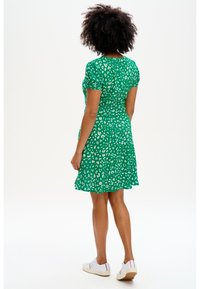 Zelené šatny s krátkým rukávem, s leopardím potiskem, rozšířeným lemem a upnutým pasem, kombinované s bílými teniskami.