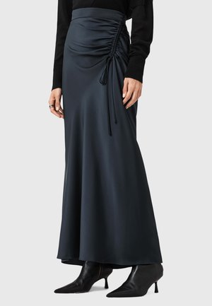 Jupe maxi en satin noir avec des détails froncés sur le côté, ornée d'un accent à cordon. Portée avec des bottes à talons aiguille noires.