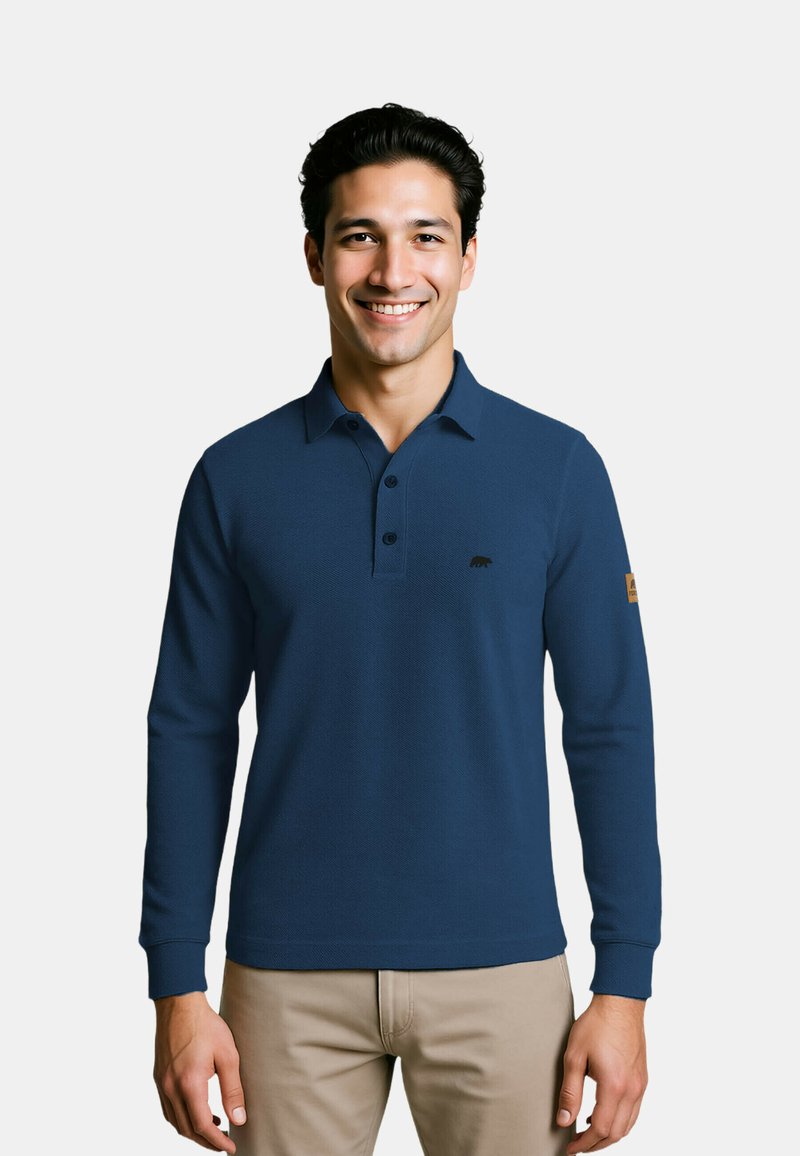 Marineblaue Langarm-Polohemd aus strukturiertem Stoff, mit Knopfleiste und kleinem schwarzem Logo auf der Brust. Neutrale beige Hose.