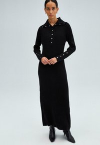 Abito nero a maglia con colletto, patta dei bottoni e maniche lunghe con dettagli in bottone argentato sui polsini. Tessuto liscio, design fino al pavimento.