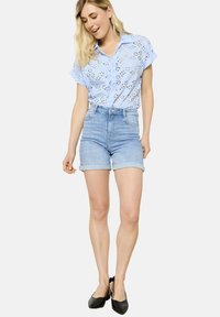 Light blue, short-sleeve button-up shirt with eyelet pattern. Paired with high-waisted, light wash denim shorts with rolled cuffs. Black shoes.