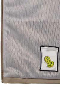 Gray mesh bag with a beige bottom, featuring an embroidered patch of a packet with two yellow smiley faces. Zipper closure along one side.