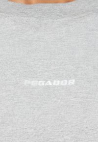 Gray sweatshirt made of soft fabric. Features a ribbed neckline and a white embroidered "PEGADOR" logo on the chest.