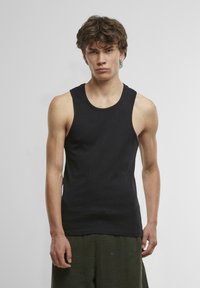 Schwarzes ärmelloses Tanktop aus Baumwolle, mit rundem Ausschnitt und figurbetontem Design, kombiniert mit grün karrierten Shorts.
