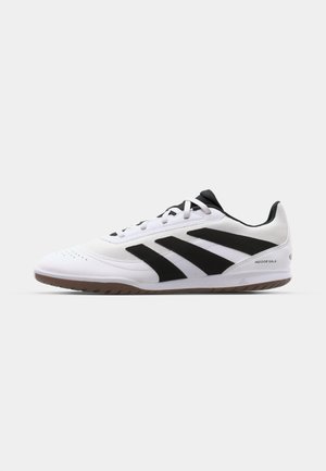 White athletic shoes featuring a textured upper, three black stripes, a smooth toe cap, and a gum rubber sole, designed for indoor use.