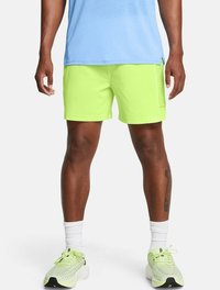 Pantalones cortos deportivos de color verde neón con una textura suave, que cuentan con bolsillos laterales y un ajuste holgado, combinados con zapatillas de deporte de color verde claro.