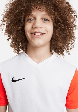 Koszulka piłkarska Nike z białym korpusem i pomarańczowymi rękawami, z dekoltem w serek oraz czarnym logo swoosh na górnej lewej części klatki piersiowej.