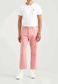 Jean droits rose clair avec cinq poches et une fermeture à bouton classique, associés à un t-shirt blanc uni et des baskets blanches.