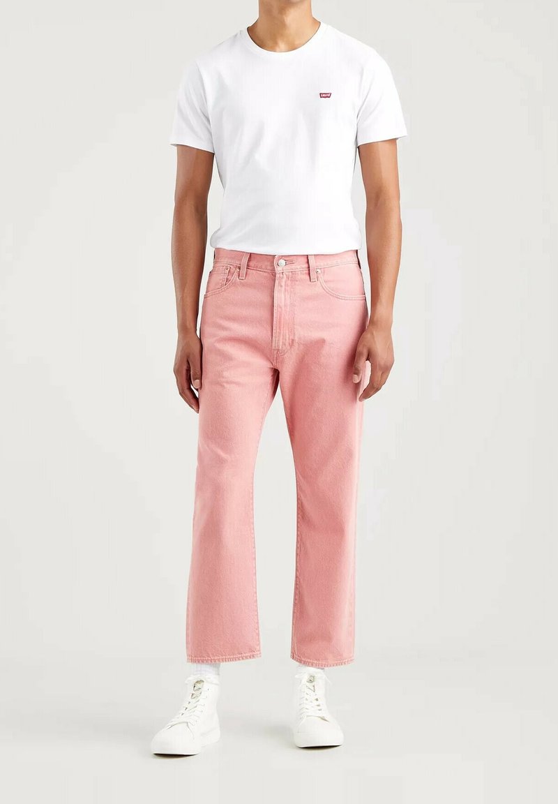 Jean droits rose clair avec cinq poches et une fermeture à bouton classique, associés à un t-shirt blanc uni et des baskets blanches.