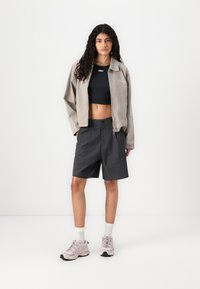 Gray corduroy jacket, black crop top, plaid shorts, and light pink sneakers. Features include a button closure and textured fabric.