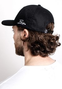 Black cap made of cotton, featuring a curved brim and white embroidered logo on the side. Adjustable strap at the back.