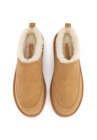 Botine din suede bej cu căptușeală moale din blană albă și o buclă pe călcâi pentru a fi ușor de purtat. Vârf rotunjit și exterior neted.