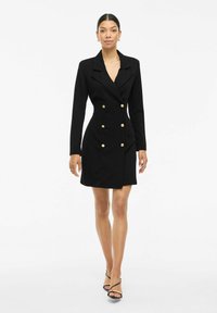 Schwarzes, doppelt knopfbares Jackenkleid mit langen Ärmeln, goldenen Knopfakzenten und figurbetonter Silhouette. Glattes Material, knielange Schnittform.
