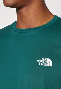Grøn bomulds t-shirt med rund hals og korte ærmer. Har et hvidt logo med et halvcirkel design på venstre bryst.