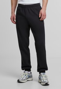 Sorte treningsbukser med elastisk midje og sidestriper. Stoffet er glatt; mansjettene er tettsittende. Kombinert med sølv- og blå sneakers.