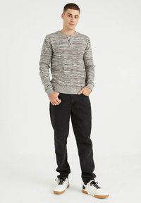 Suéter gris de punto con un patrón texturizado, cuatro botones en el cuello, combinado con pantalones negros y zapatillas blancas con suelas de goma.