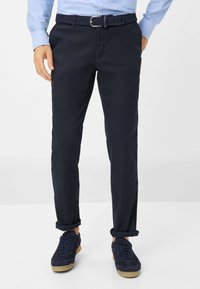 Marineblauwe katoen chinos met een rechte pasvorm, details op de zakken, opgerolde mouwen en gecombineerd met donkerblauwe suède sneakers.