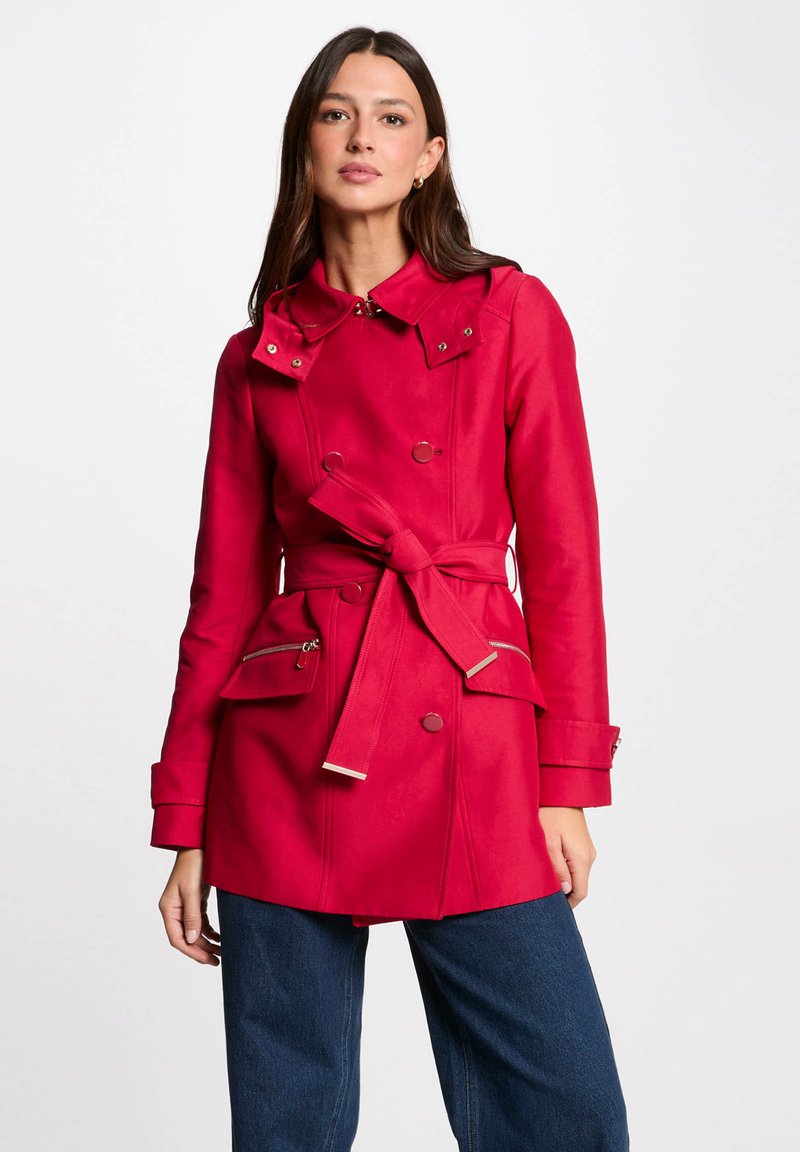 Trench coat rosso con vita sottile, frontale doppiopetto, grande colletto e due tasche con zip; realizzato in tessuto liscio e strutturato.