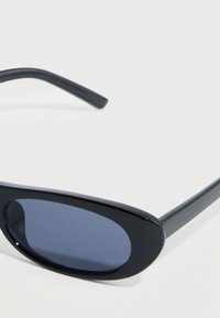 Μαύρα οβάλ γυαλιά ηλίου με σκούρους φακούς. Το πλαίσιο είναι από λείο πλαστικό με λεπτούς, καμπυλωτούς βραχίονες. Χωρίς ορατά λογότυπα ή σχέδια.