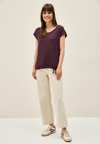 Haut courte à manches maroon avec un ourlet à cordon de serrage, assorti à un pantalon large écru et des baskets beiges avec des accents rouges.