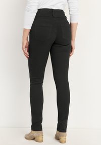 Mustat korkeat farkut takataskuilla, joissa on slim fit ja sileä pinta. Yhdistetty vaaleanbeigeihin korkokenkiin.