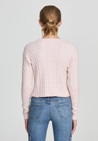 Pullover rosa a maglia con maniche lunghe, design corto e polsini a costine, abbinato a jeans in denim di lavaggio medio.