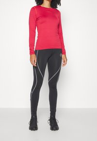Punainen pitkähihainen urheilu頂上, jossa on teksturoitu kangas ja oranssit yksityiskohdat, yhdistettynä mustiin legginsseihin, joissa on harmaat sivuviivat ja logo. Mustat kengät ovat päällä.