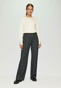 Crème blouse met een ronde halslijn en een middennaad, gecombineerd met hoge, wijdvallende trousers in een donker geruit patroon. Zwarte chunky schoenen.