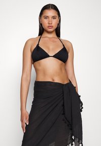 Melna bikini blūze ar ribota tekstūru un sasienamām saitēm, kopā ar saskaņotu melnu apakškleitu ar pušķu akcentiem gar apakšu.