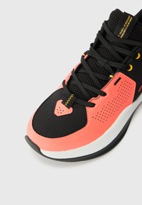 Sort og pink sportsko med en mesh-overdel, teksturerede detaljer og rund tå. Har kontrastsnørebånd og en hvid sål med sort kant.