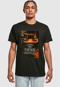 Sort bomulds t-shirt med et trykt grafisk motiv af en kvindes øjne og tekst. Designet indeholder røde og grønne accentelementer.