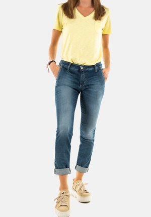 Camiseta amarilla de cuello en V, jeans de mezclilla con un lavado claro, puños enrollados y zapatillas de plataforma beige con cordones. Incluye bolsillos frontales.