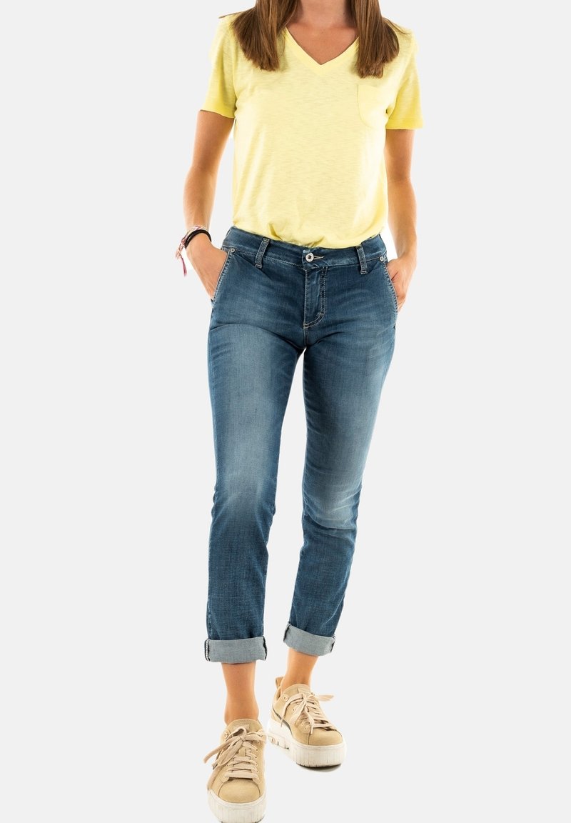 Camiseta amarilla de cuello en V, jeans de mezclilla con un lavado claro, puños enrollados y zapatillas de plataforma beige con cordones. Incluye bolsillos frontales.