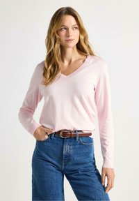 Lyserød v-hals sweater i blødt stof med lange ærmer og ribkant. Kombineret med højtaljede blå jeans og et brunt bælte.