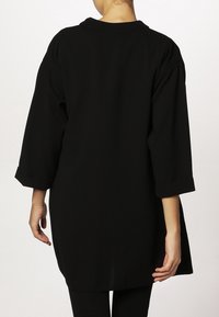 Černý př oversized top s tříčtvrtečními rukávy, kulatým výstřihem a hladkou texturou. Má rovný lem a žádné viditelné vzory nebo akcenty.
