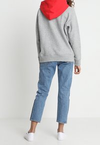 Sweat-shirt gris avec capuche rouge, associé à un jean bleu droit. Des baskets blanches complètent le look, offrant une coupe décontractée et confortable.