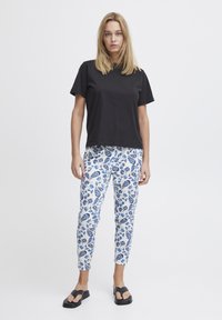 Zwarte, kortärmelige t-shirt gecombineerd met witte en blauwe bloemenpatroon broek. Model draagt donkere sandalen. Eenvoudig, casual kledingontwerp.