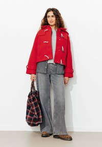 Manteau court rouge en duffle avec des accessoires en argent, pull gris, jean gris à jambes larges et sac fourre-tout à carreaux. Des chaussures à imprimé animal complètent la tenue.