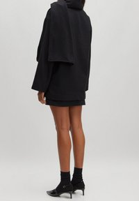 Musta ylisuuri collegepaita, jossa on korkea kaulus, yhdistetty mustaan minihameeseen, mustiin sukkiin ja mustiin korollisiin kenkiin. Pehmeä materiaali, minimalistinen muotoilu.