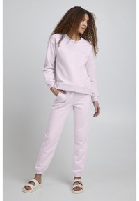 Lichtroze katoenen sweatshirt met geribde manchetten en zoom, met de tekst "The Fogg Concept". Gecombineerd met bijpassende roze joggers en witte sandalen.