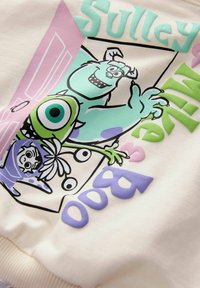 Tessuto color crema con grafiche di cartoni animati multicolori di Sulley e Mike da "Monsters, Inc." Include accenti di testo giocosi.