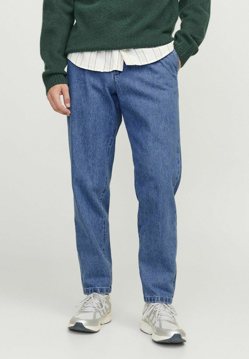 Jeans de mezclilla azul claro con un corte recto, que presentan un diseño clásico de cinco bolsillos y un ligero desgaste. Combinados con un suéter de punto verde.