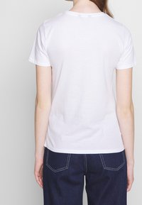 Camiseta de algodón blanca con cuello redondo y mangas cortas. La vista trasera muestra una textura suave y una forma ajustada.