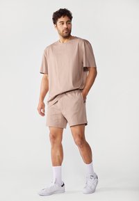 Korte mouwen, beige t-shirt met een relaxte pasvorm, gecombineerd met bijpassende shorts. De outfit heeft een zachte stof en zijzakken, aangevuld met witte sneakers.