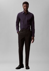 Dark purple button-up shirt and black tailored trousers. The shirt has long sleeves and a fitted silhouette; shoes are black leather.