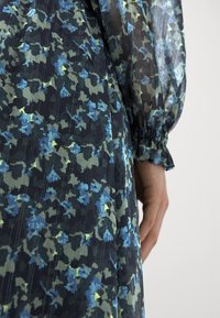 Durchsichtiges Kleid aus dunklem Stoff mit einem blauen und grünen Blumenmuster. Verfügt über elastische Bündchen und eine vertikale Streifenstruktur.