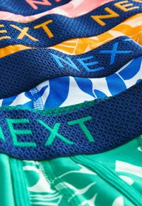 Bralettes en tissu coloré avec divers motifs. Présentent des bretelles texturées en bleu foncé, avec un lettrage de marque contrastant en orange et vert.