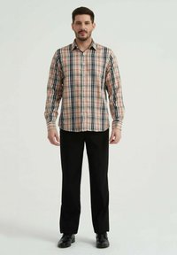 Chemise à carreaux beige, noir et rouge avec des manches longues et une fermeture à boutons, assortie à un pantalon noir et des chaussures noires.